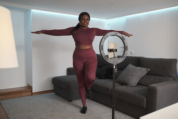 African young woman vlogger records yoga tutorials or virtual fitness class with her phone at home.