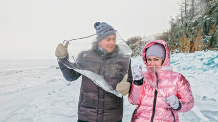 Couple has fun winter walk against background of ice of frozen lake. Lovers lie on clear ice with...