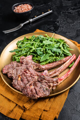 BBQ grilled lamb cutlet or mutton chop steak with arugula salad on a plate. Black background. Top...