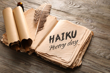 Open old book with text HAIKU POETRY DAY and feather with scrolls on wooden background