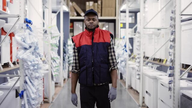 Salesman walking between rows in hardware store, looking to the camera