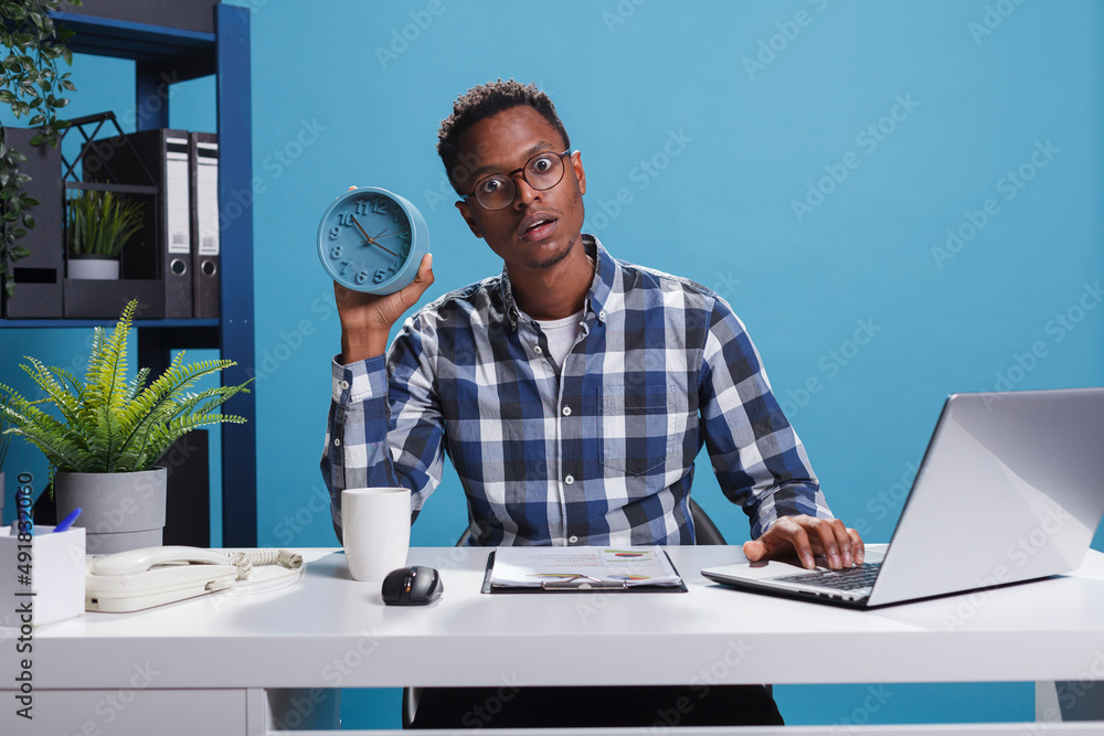 Poster company businessman with shock expression face having alarm clock while using work laptop. perplexed