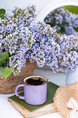The postcard is beautiful. A fancy purple coffee mug, an old book, a straw hat and a bouquet of purple lilac. Beautiful still life. Spring time. The concept of 