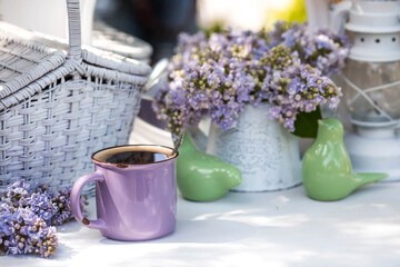 The postcard is beautiful. A fancy purple coffee mug, an old book, a straw hat and a bouquet of purple lilac. Beautiful still life. Spring time. The concept of "Good morning".
