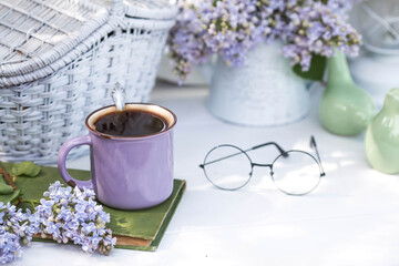 The postcard is beautiful. A fancy purple coffee mug, an old book and a bouquet of purple lilac. Beautiful still life. Spring time. The concept of 