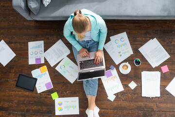 Young woman works with documents using a laptop while sitting on the floor at home. Student, entrepreneur or freelancer girl working or studying remotely via internet.