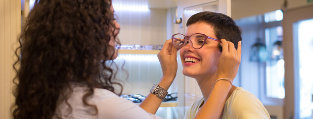 Two young women buying eyeglasses in optical shop