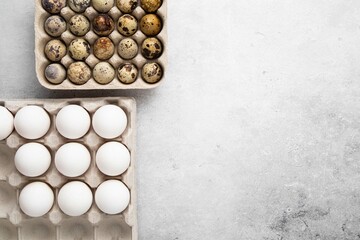 Different kinds of bird eggs in paper tray. White chicken and quail eggs on light background. Top view, copy space or empty place for text.