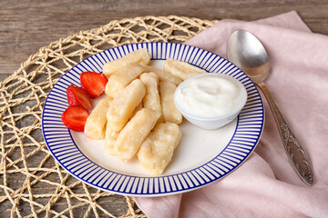 Plate with delicious lazy dumplings and sour cream on wooden background