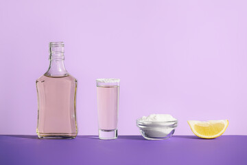 Bottle and glass of tasty tequila, salt and lemon on color background