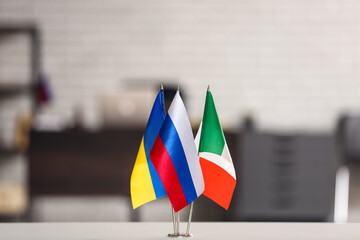 Ukrainian, Russian and Italian flags on table against blurred background