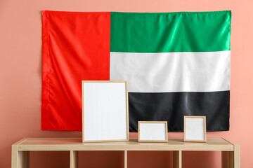 Shelf with blank frames and UAE flag hanging on pink wall