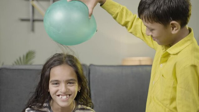 Kids enjoys static cling experiment by playing while rubbing ballon to hair and hairs attracted to ballon - conept of excitement and home science experiment.