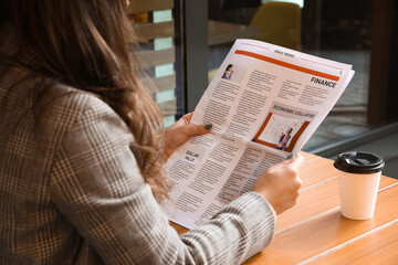 Naklejka premium Young woman reading newspaper at table in cafe, closeup