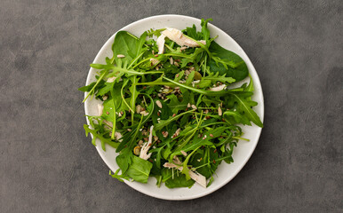 Delicious light salad with arugula and chicken breast sprinkled with various healthy seeds in a plate on a gray background, top view