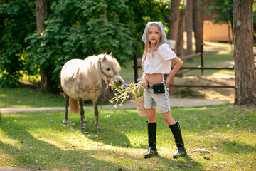 Tween girl standing in summer country estate with grazing horse on background
