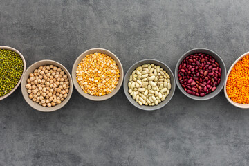 Different types of legumes in bowls, yellow peas and chickpeas , colored beans and maash and lentils, top view, copy space