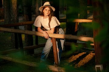 Teenage girl standing in country estate in forest in rays of setting summer sun