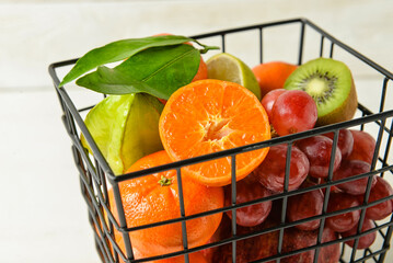 Basket with juicy fruits on white wooden background, closeup