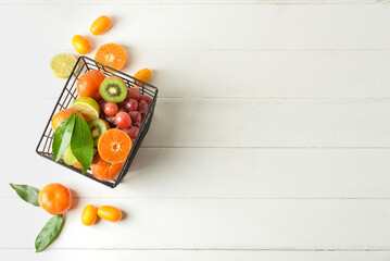 Naklejka na ściany i meble Basket with juicy fruits on white wooden background