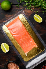 Vacuum packed salmon portion fillet, with herbs, on old dark  wooden table background, top view...