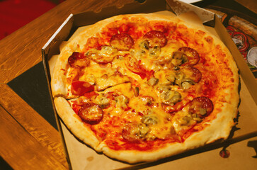 Appetizing hot pizza with sausage and mushrooms in tomato sauce. Pizza in a cardboard box.