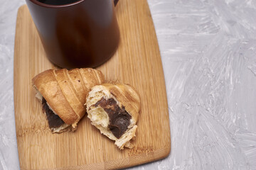 a coffee mug and a croissant broken in half on a cutting board