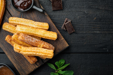 Fototapeta na wymiar Churros with caramel Traditional Spanish cusine, on black wooden table background, top view flat lay with space for text, copyspace