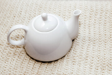Teapot with tea on the background of natural warm knitted fabric pattern.