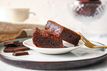 Plate with pieces of delicious chocolate brownie on light background
