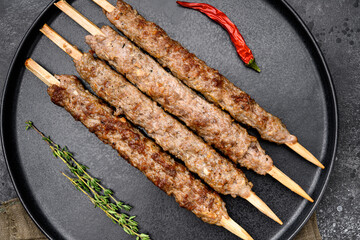 Mutton kebab shish skewers, on plate, on black dark stone table background, top view flat lay