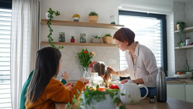 Mother of three little children preparing breakfast in kitchen at home.