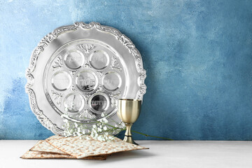 Passover Seder plate with cup of wine and matza on table against color background