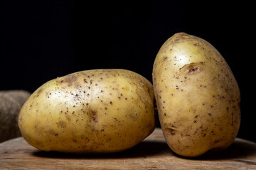 Young potatoes on a black background. Raw yellow potatoes. New crop