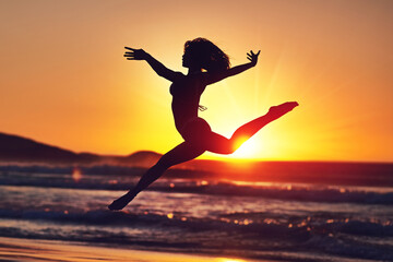 Sometimes you have to let go and be free. Silhouette of an energetic woman jumping on the beach at...