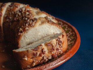 Slices of sweet bread with pieces of walnuts on top, over a mud or clay Mexican plate and a blue surface table, side view macro photography.