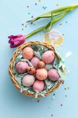 Basket with painted Easter eggs, card with text HAPPY EASTER and tulip flower on blue background