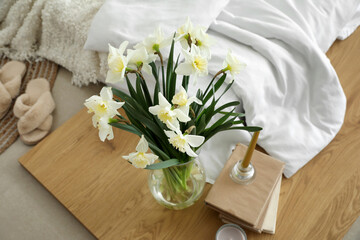 Vase with daffodils, books and candles on board in bedroom