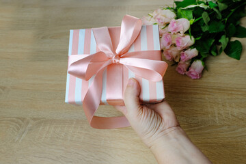 closeup female hands holding a box with gift, bouquet of white, pink roses, box with gift with satin ribbon, flowers for professional holiday, concept of mother's, Valentine's day, birthday