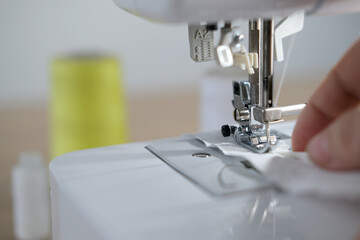 close-up of female hands perform work on a white sewing electric computer machine, stitches appear step by step on the fabric, concept of tailoring, women's hobby, modern needlework