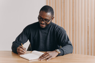 Young african american man entrepreneur in glasses taking notes in agenda