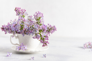 Decorative composition with Bouquet of lilacs in a porcelain cup on light background. lilacs branches in vase. Spring floral background with lilacs. Copy space. Poster, greeting card design