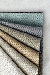 Fabric swatches in different colors are stacked for selection. A variety of shades of upholstery material for furniture and interior. Fabric texture close up. A set of multi-colored rolls of material
