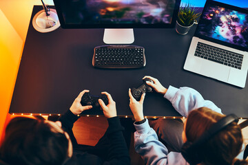 Friends playing video game at home. Gamers holding gamepads sitting at front of screen. Streamers...