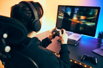 Man playing video game at home. Gamer holding gamepads sitting at front of screen. Streamer playing online in dark room lit by neon lights. Competition and having fun