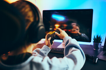 Teenager girl playing video game at home. Gamer playing online in dark room lit by neon lights. Competition and having fun