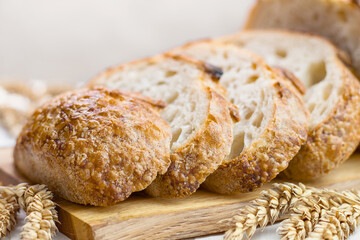 Slices of freshly baked bread with ears of wheat on wooden board on table, selective focus.