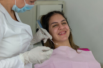 Smiling teenager girl with braces having dental treatment at dentist's office