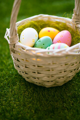 Vertical Easter background with colorful yellow, pink, blue Easter eggs in woven basket and green grass. Top view with copy space. Easter holidays social media background.