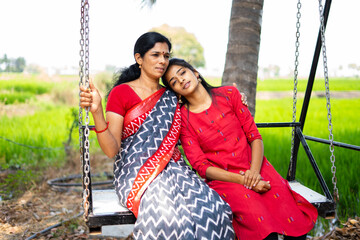 Mother and daughter relaxing on swing while on outside - concept of family bonding, affection and...